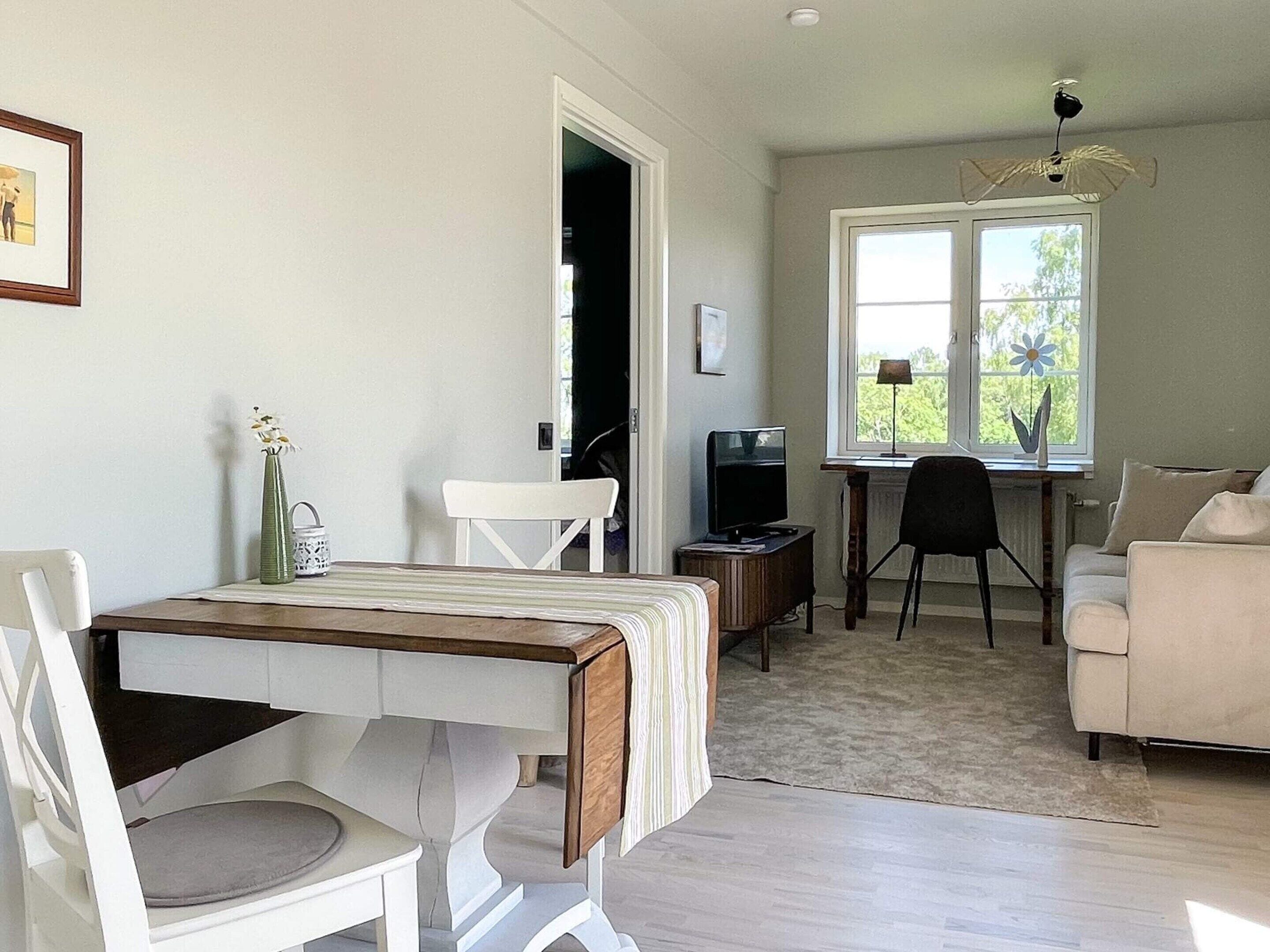 A room with a dining table, chairs, a sofa, a TV, and a window with a view.