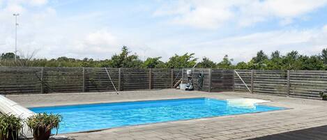 A rectangular swimming pool with a wooden deck surrounding it, a wooden fence, and potted plants.