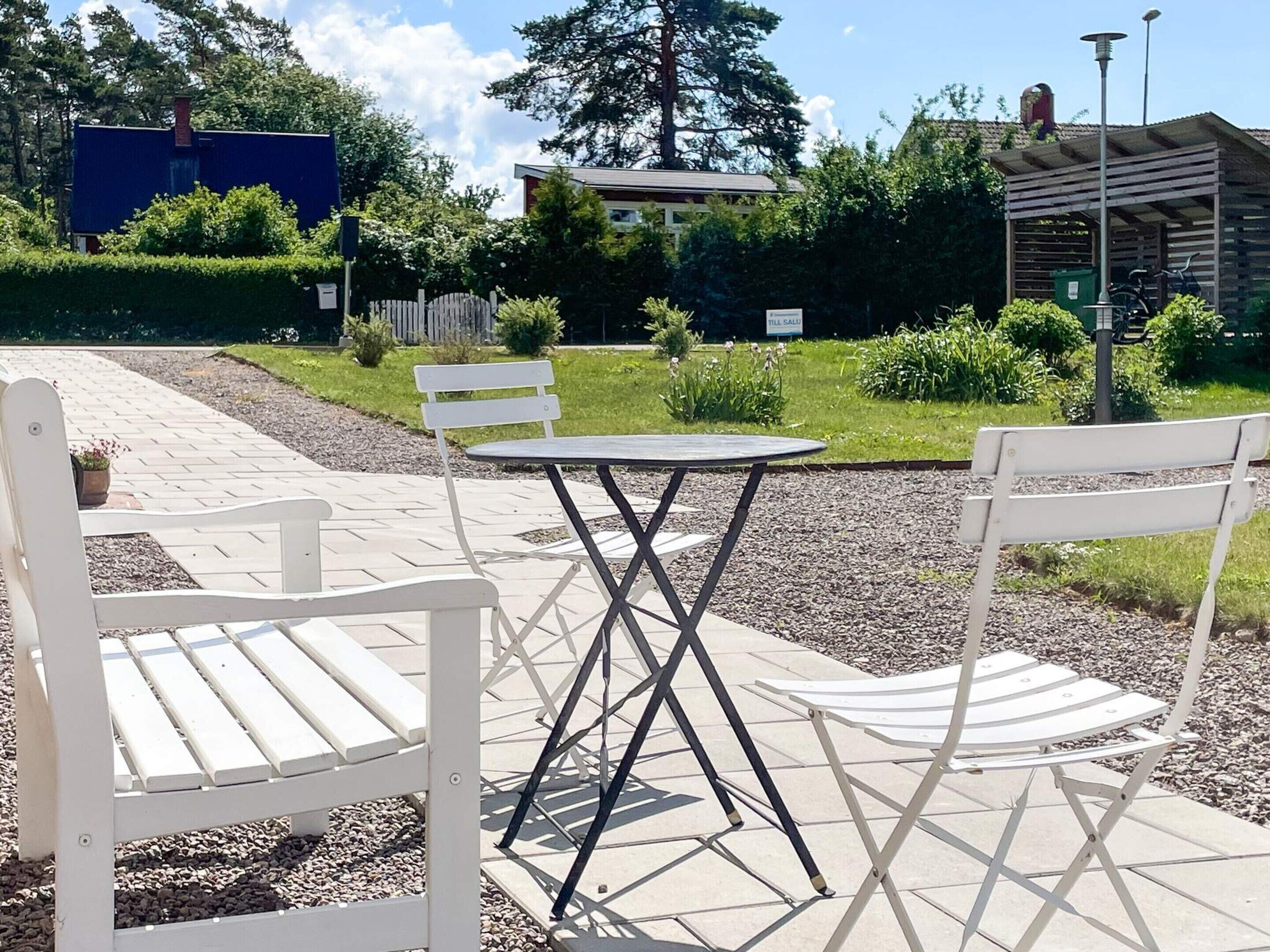 Un patio con sillas y una mesa blancas, rodeado por un jardín con un cartel de 'TILL SALE'.