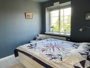Ein Schlafzimmer mit einem Bett, einem Fenster mit Blick, einer Lampe und einem gerahmten Bild an der Wand.