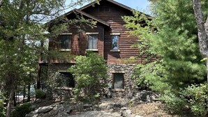 A rustic wooden cabin with a stone foundation, surrounded by dense forest. - Stonewater 2br BLOCK (Shell Knob)