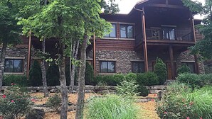 A multi-story log cabin with stone accents, a balcony, and a landscaped garden with various plants and shrubs. - Stonewater 2br BLOCK (Shell Knob)