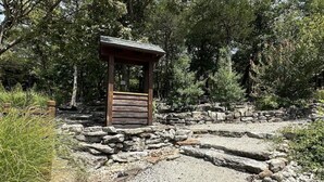 A rustic wooden structure with a stone pathway leading to it, surrounded by dense greenery. - Stonewater 2br BLOCK (Shell Knob)