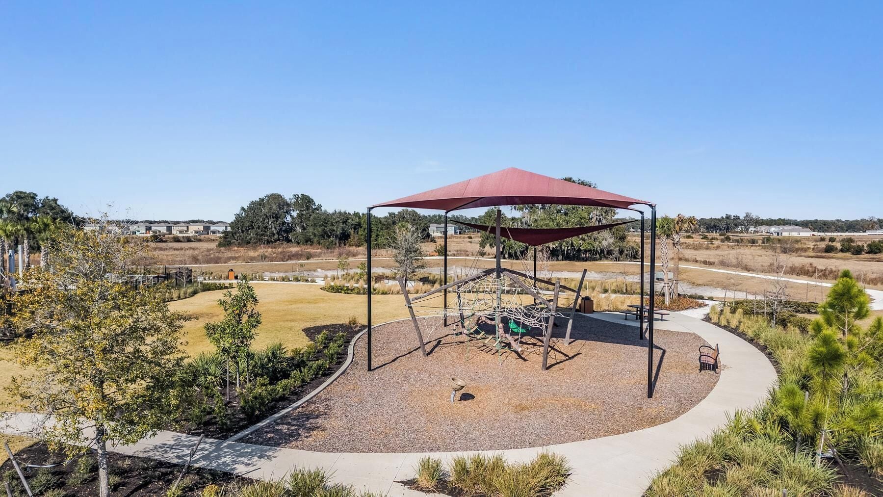 A playground with a swing set and a climbing structure, surrounded by a gravel area and trees.