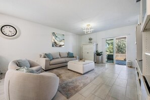 A modern living room with a sofa, a coffee table, a cabinet, and a large window. - 5 BR Home/Sleeps 10/3 Offices/Fenced/Garage (Zephyrhills)