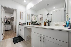 Ein modernes Badezimmer mit großem Spiegel, weißen Schränken und einem Schminktisch.