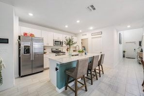 Uma cozinha moderna com eletrodomésticos de aço inoxidável, uma ilha central com banquetas e um esquema de cores branco.