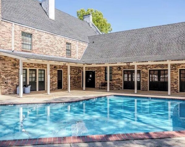 A poolside area with a brick building, a covered patio, and a swimming pool. - Lovely 2-bedroom Townhome, Baton Rouge (Baton Rouge)