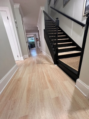 A hallway with a wooden floor, a black staircase, and a door at the end. - Lovely 2-bedroom Townhome, Baton Rouge (Baton Rouge)
