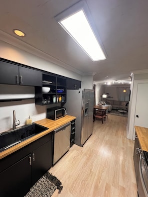 A modern kitchen with black cabinets, a stainless steel refrigerator, a microwave, and a wooden countertop. - Lovely 2-bedroom Townhome, Baton Rouge (Baton Rouge)