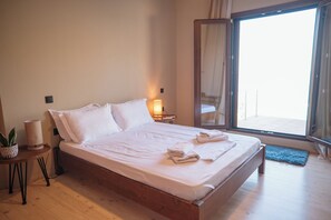 Un dormitorio con una cama grande, una lámpara de noche, una mesita con una planta y vistas a un espacio exterior a través de un ventanal.
