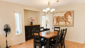 A dining area with a wooden table, black chairs, a chandelier, and a large abstract painting on the wall.