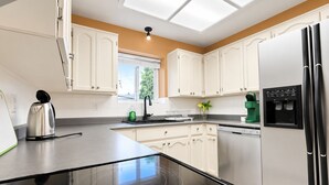 A modern kitchen with white cabinets, a black countertop, a built-in dishwasher, and a refrigerator with a water dispenser.