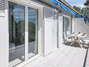 Eine Terrasse mit Tisch und Stühlen, eine Schiebetür und ein blaues Markisenvorzelt.