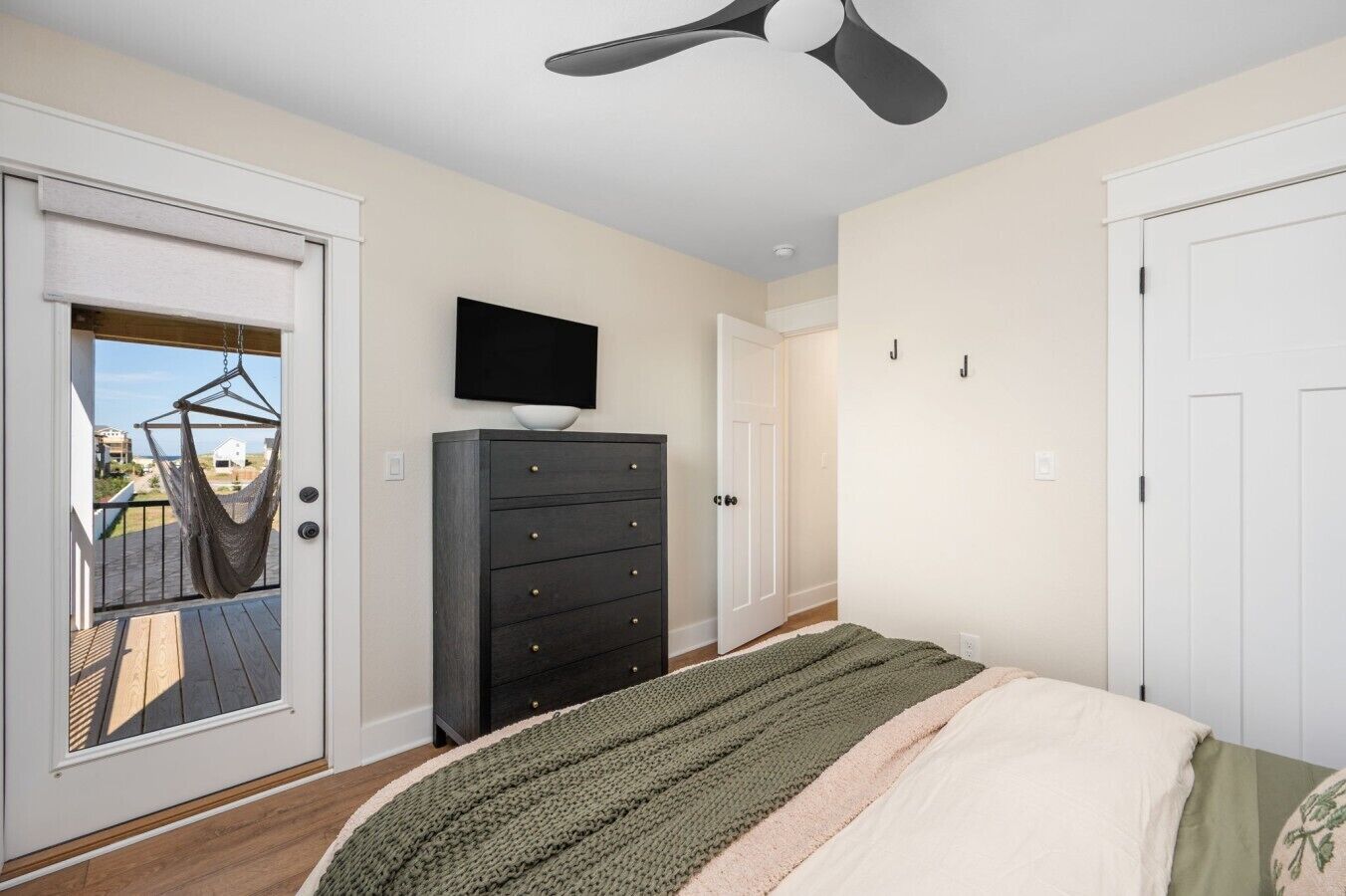 A bedroom with a bed, a dresser, a television, and a balcony door.