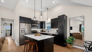 Uma cozinha moderna com armários escuros, uma ilha central, eletrodomésticos de aço inoxidável e vista para a área de estar.