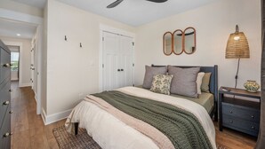 Quarto com cama, ventoinha no teto, mesa de cabeceira, abajur e cômoda.