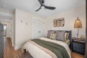Ein Schlafzimmer mit Bett, Deckenventilator, Nachttisch, Lampe und Kommode.