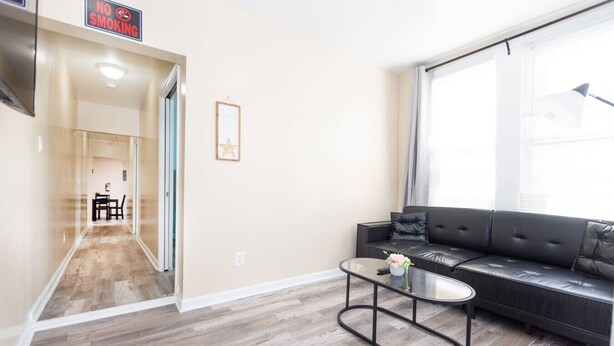 A modern living room with a sofa, coffee table, and a hallway leading to a dining area. - Modern 2BR Near Beach | Full Kitchen & Parking (Wildwood)