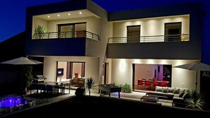 Una casa moderna de dos pisos con balcón, mobiliario exterior y zona de barbacoa.