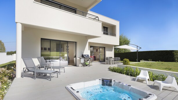 Une maison moderne à deux étages dotée d’un patio, d’un espace salon extérieur et d’un jacuzzi.