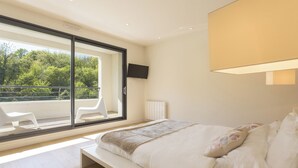 Une chambre avec une grande fenêtre, un lit, une chaise et un téléviseur.