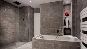 Une salle de bain moderne dotée d’une douche à l’italienne, d’une baignoire sur pieds et d’une étagère où sont rangés les articles de toilette.