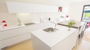 Une cuisine moderne avec des meubles blancs, un îlot central doté d’un évier et une vue sur l’extérieur.