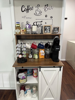 Una cafetería con un letrero que dice 'Coffee & Tea BAR', una cafetera Keurig y diversos productos de café y té.