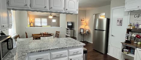 A kitchen with white cabinetry, a granite countertop, a stainless steel refrigerator, and a coffee station.