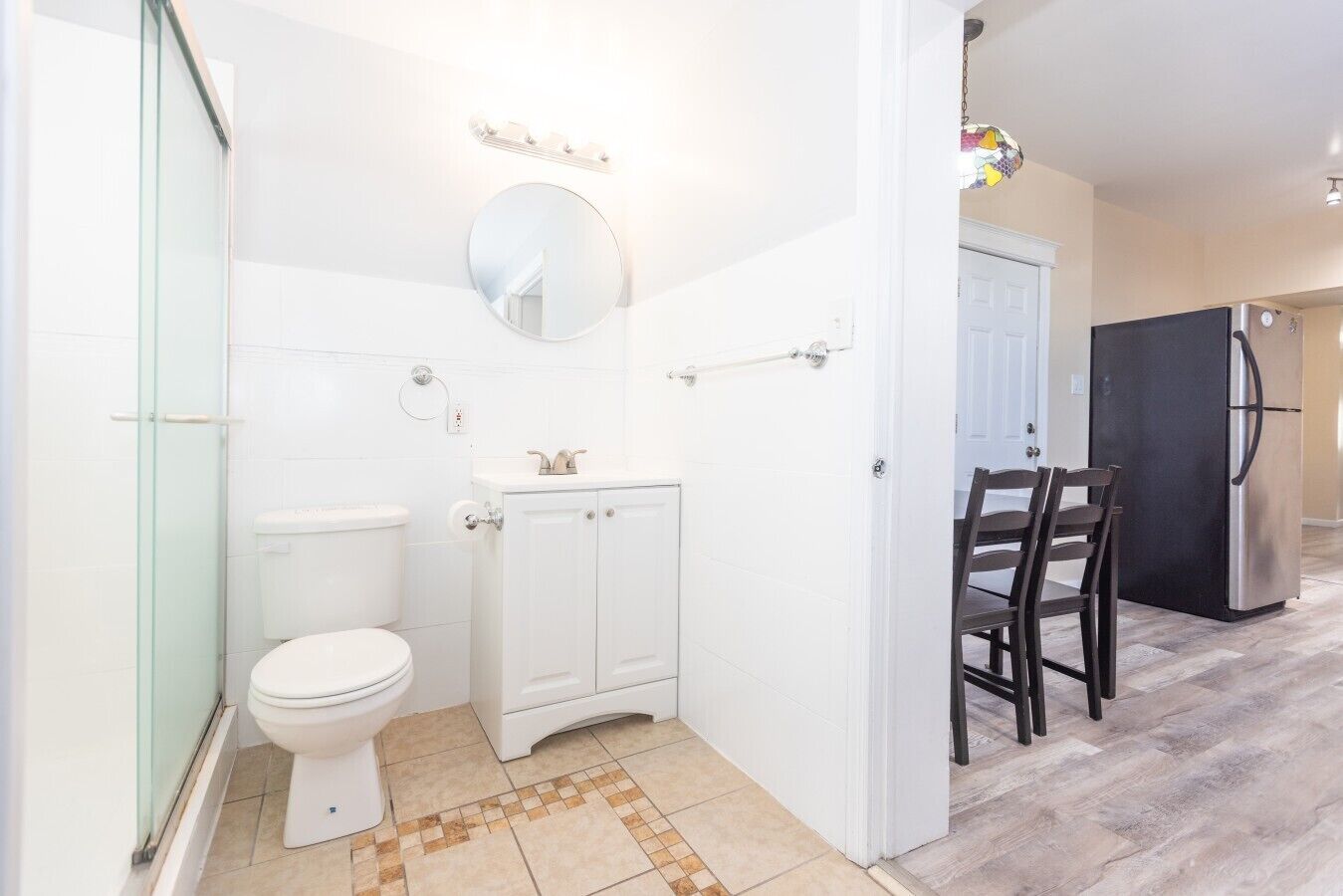 Une salle de bain comprenant des toilettes, un lavabo et un miroir, une douche en verre, ainsi qu’un coin repas avec une table et des chaises.