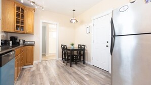 Una cocina con armarios de madera, un refrigerador de acero inoxidable, una mesa de comedor con sillas y una lámpara colgante.