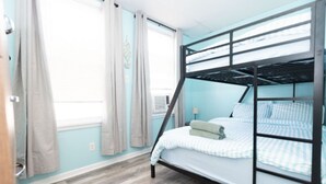 Dormitorio con literas, ventana, cortinas y suelo de madera.