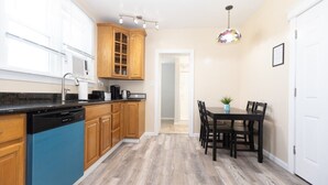 Una cocina con armarios de madera, lavavajillas, cafetera y una mesa de comedor con sillas.