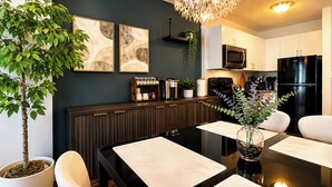 Una cocina moderna con armarios oscuros, un refrigerador negro, un microondas y una cafetera. Hay una mesa de comedor con sillas y un florero con plantas verdes.