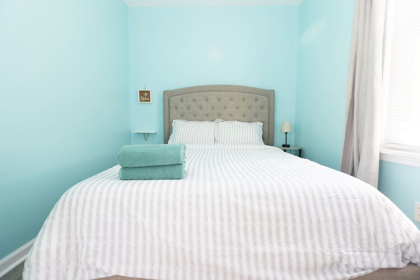 Una cama bien hecha con ropa de cama a rayas, un cabecero y una toalla doblada sobre la cama.