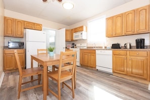 A kitchen with wooden cabinets, a dining table with chairs, a microwave, a refrigerator, a dishwasher, and a coffee maker. - Coastal Breezes 2BR | Upper Balcony (Wildwood)
