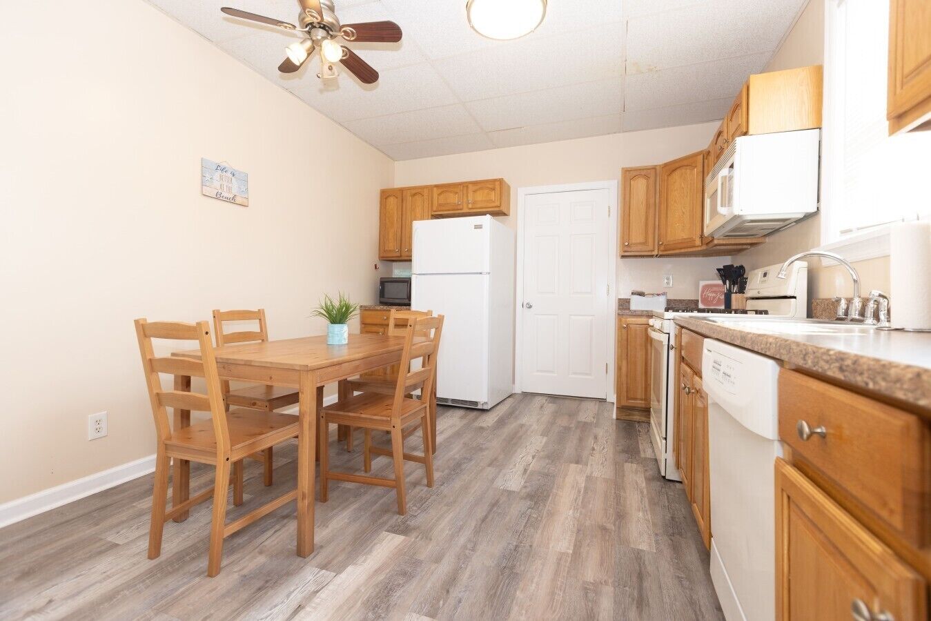 Una cocina con armarios de madera, un refrigerador blanco, un microondas, un lavavajillas y una mesa de comedor con sillas.