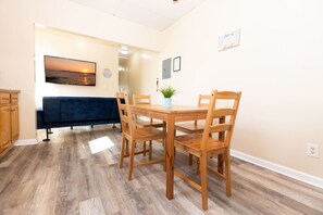 A dining area with a wooden table and chairs, a blue sofa, and a wall-mounted TV. - Coastal Breezes 2BR | Upper Balcony (Wildwood)