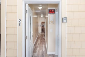 A hallway with a 'No Smoking' sign, a framed picture on the wall, and a door with the number '2R' visible. - Coastal Breezes 2BR | Upper Balcony (Wildwood)