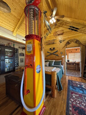 Interior rústico de cabaña con una bomba de gasolina antigua, paredes de madera, una cama y esquíes.