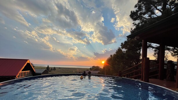 En pool med utsikt över solnedgången, ett trädäck och en byggnad med ett rött tak.
