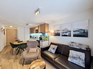 Ein modernes Wohnzimmer mit einer Couch, einem Esstisch mit Stühlen, einer Küchenzeile und Kunstwerken an den Wänden.