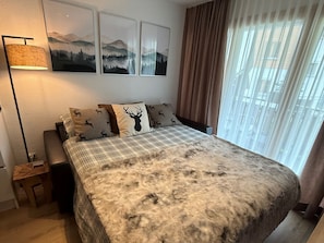 Ein Schlafzimmer mit Bett, Nachttisch, Lampe, einem Fenster mit Vorhängen und Wandbildern.