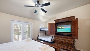 Une chambre à coucher comprenant un lit, une commode, un téléviseur et un ventilateur de plafond.