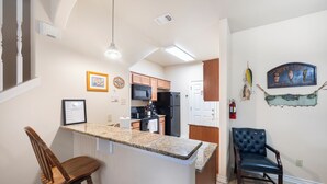 Une cuisine dotée de plans de travail en granit, de meubles en bois, d’un réfrigérateur noir et d’un tabouret de bar.