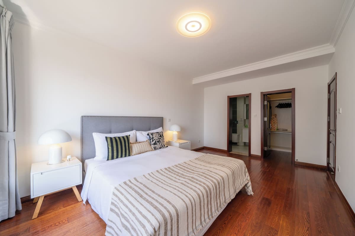 Ein Hotelzimmer mit einem großen Bett, zwei Nachttischen mit Lampen, Holzboden und einer Tür zu einem Badezimmer.