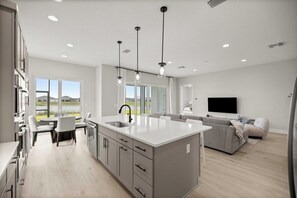 Eine moderne Küche mit Kochinsel, Essbereich und Wohnzimmer mit Sofa und Fernseher.