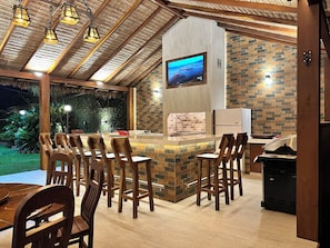 Un espace bar extérieur avec des chaises en bois, un écran de télévision et un mur en briques.