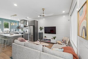 Une cuisine moderne avec un îlot central, un coin repas avec un canapé et un téléviseur fixé au mur.